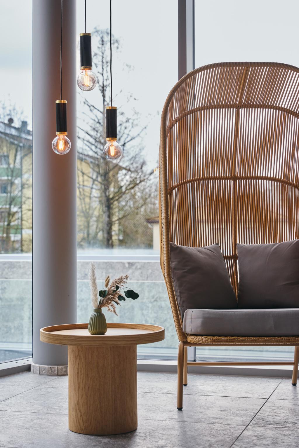 Gemütlicher Sitzkorb mit grauen Polstern und Beistelltisch aus hellem Holz mit Trockenblumen in der Skylounge des Hotel Holzapfel
